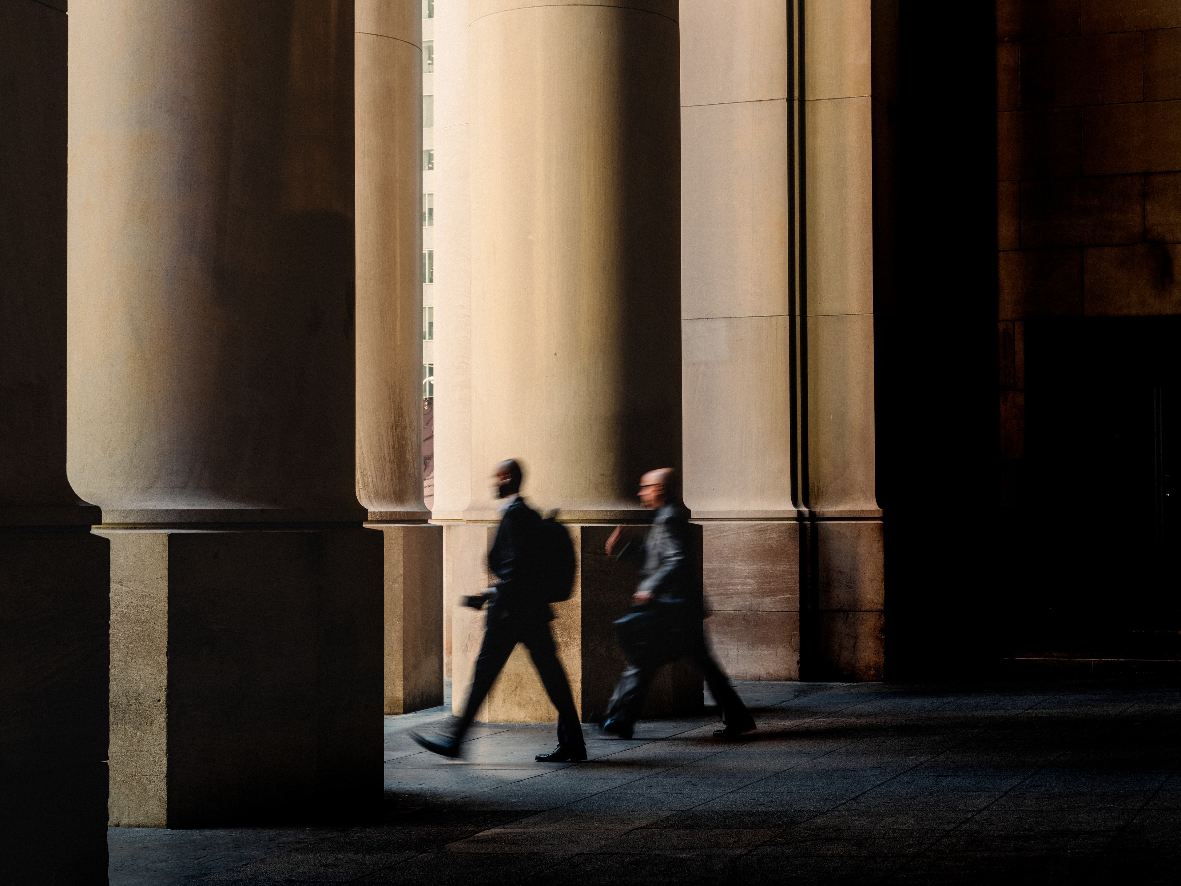 Two men walking past large columns into the sun with a motion blur effect